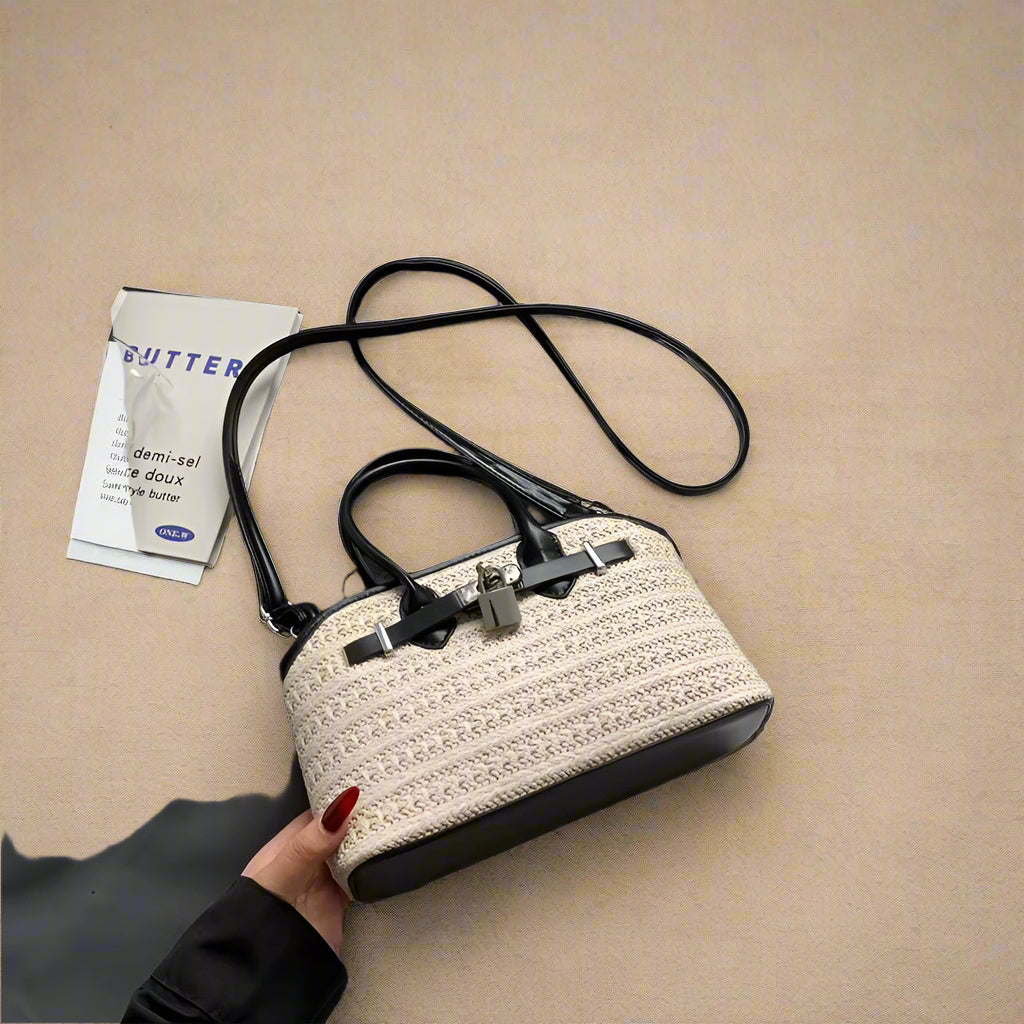 Handbag with textured design held by a hand on a white surface with a gray garment and book in the background.