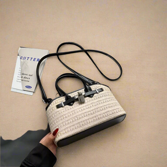 Handbag with textured design held by a hand on a white surface with a gray garment and book in the background.